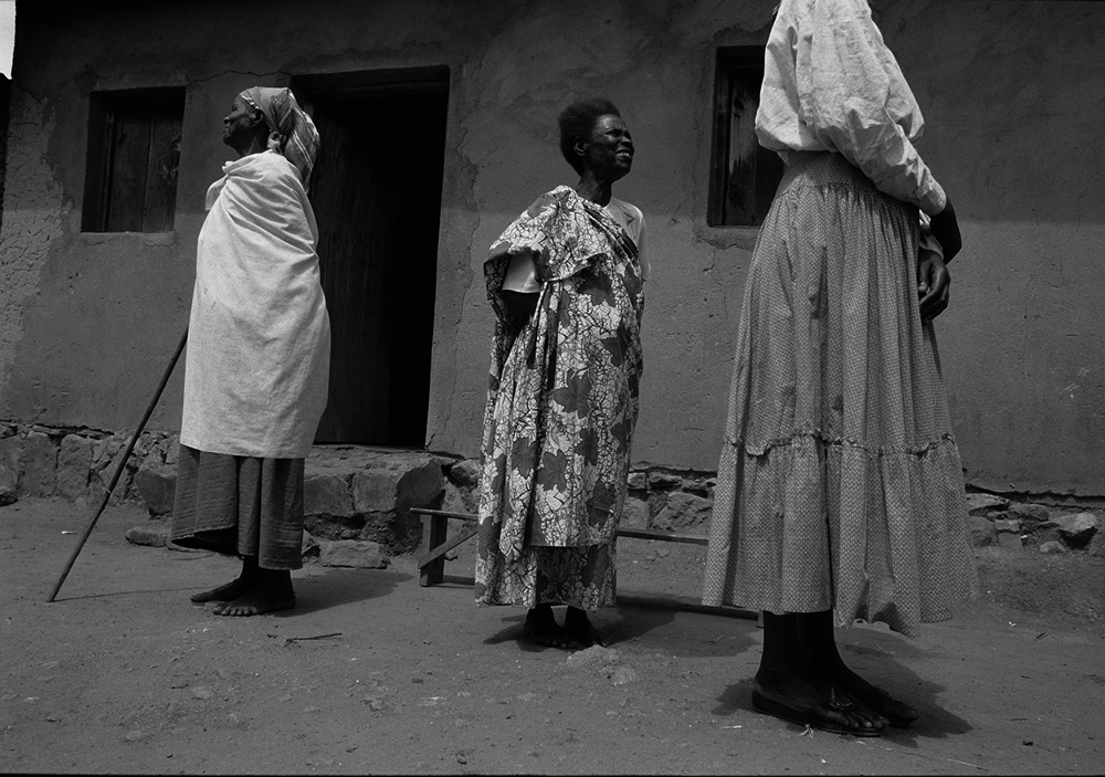 A black and white photo of three women standing in front of a home in Rwanda.