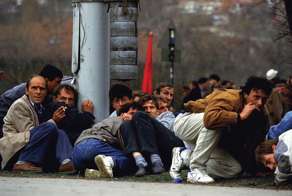 A group of men huddles on the ground, looking upward at something out of the frame of the photo.