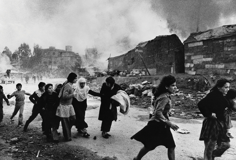 Black and white photo of people fleeing, with smoke and rubble in the background.