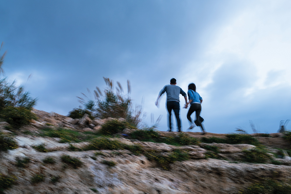 Blurry photo of a young man and woman running up a hill. The photo is taken from the foot of the hill beneath them.