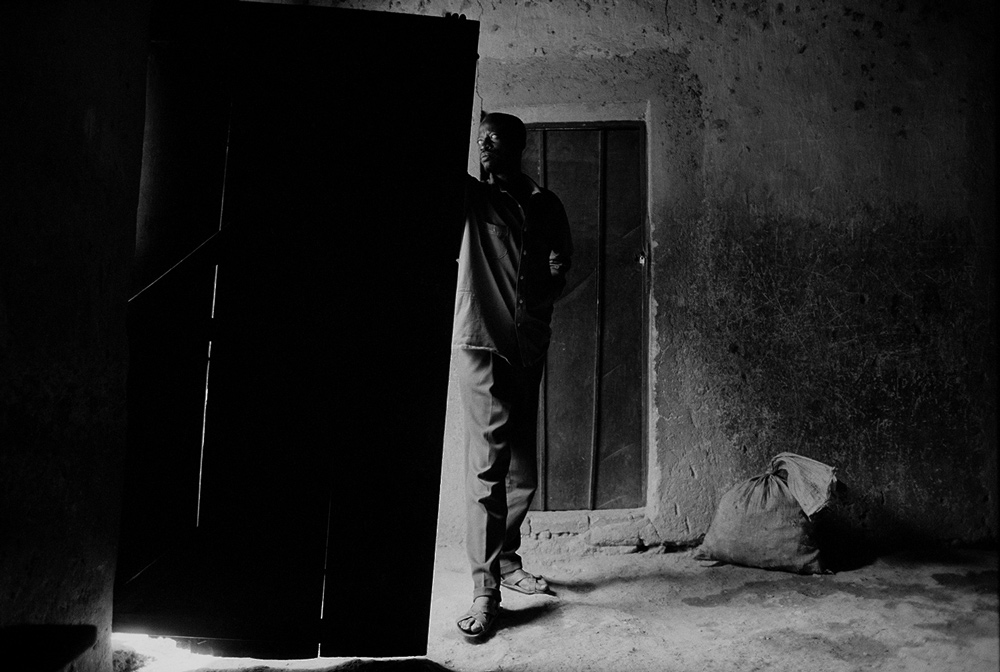 A black and white photo of a man standing inside a building, looking out to his right through an open doorway.